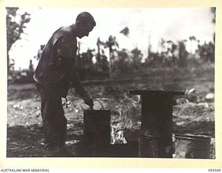 CAPE WOM, WEWAK AREA, NEW GUINEA, 1945-08-24. PRIVATE SAWYER, 2/119 BRIGADE WORKSHOP CORPS OF AUSTRALIAN ELECTRICAL AND MECHANICAL ENGINEERS WITH HIS NOVEL WATER-HEATER. IT IS FUELLED BY HALF ..