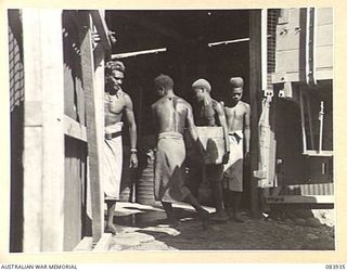 LAE, NEW GUINEA. 1944-12-12. NATIVES SUPPLIED BY ANGAU UNLOAD A TRUCK OF EMPTY BOTTLES UNDER THE SUPERVISION OF AN ARMY CANTEENS SERVICE DRIVER AT A SOFT DRINK FACTORY WITHIN LAE BASE SUB-AREA