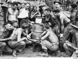 Troops of Headquarters, 7th Australian Division gathered around a radio set to listen to the running of the Melbourne Cup. Shown are: (back, standing, left to right) SX2325 K E Tamke, 2/10th ..