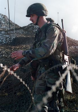 Specialists Antonio Henry US Army (USA), 1ST Battalion, 17th Infantry Division carries his 5.56mm M16A2 assault rifle as he helps to set up communication equipment at Orote Point, Guam during Exercise TANDEM THRUST '99