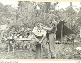 MALMAL, JACQUINOT BAY, NEW BRITAIN. 1944-11-13. THE LOCAL BARBER AT WORK IN THE CAMP OF THE 14/32ND INFANTRY BATTALION. IDENTIFIED PERSONNEL ARE:- VX120883 PRIVATE A.E. CURTIS "A" COMPANY BARBER ..