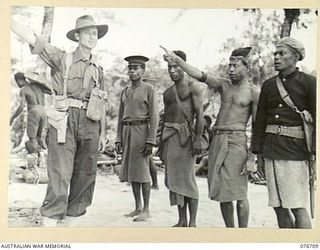 JACQUINOT BAY, NEW BRITAIN. 1944-11-06. NX151701 CAPTAIN H. LYON, OFFICER- IN- CHARGE, B COMPANY, 1ST NEW GUINEA INFANTRY BATTALION, QUESTIONING NATIVE CHIEFS (TULTULS AND LULULAIS) AND AULPAK, ..