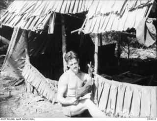 BOUGAINVILLE, 1945-06-07. SGT HUNGERFORD, READING OUTSIDE HIS HUT AT B TROOP HEADQUARTERS, 2/8 COMMANDO SQUADRON, NAIRONA VILLAGE. THE TROOPS REST IN THE CAMP BETWEEN HARASSING RAIDS ON THE ..