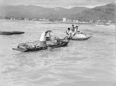 [Man in a canoe holds up a fish and people paddle in other canoes]