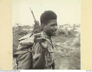 SINGORKAI - WEBER POINT AREA, NEW GUINEA, 1944-03-21. SEBUT, A MEMBER OF "C" COMPANY, PAPUAN INFANTRY BATTALION, CARRIES HIS RIFLE IN WHAT HE THINKS IS THE MOST COMFORTABLE POSITION. NOTE THE ..