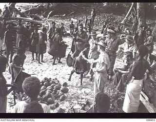 KOIL ISLAND, NEW GUINEA, 1945-10-31. CAPTAIN N. B. FOGARTY, RED CROSS REPRESENTATIVE, 6TH DIVISION, BARTERING WITH THE NATIVES FOR FRUIT IN EXCHANGE FOR COLOURED BAGS AND CLOTH. THE FRUIT IS FOR ..