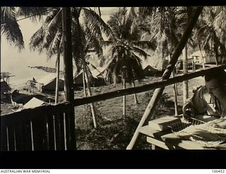 Yule Island, New Guinea. c. 1944-05-15. Lieutenant (Lt) W. R. Burgess, Officer in Charge, 1 Marine Food Supply Platoon, working in his office overlooking the camp area. Lt Burgess nickname was ..