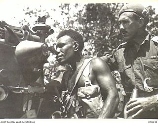 BOUGAINVILLE ISLAND. 1945-01-25. QX14582 LIEUTENANT J. MARTIN, "A" COMPANY, 1ST NEW GUINEA INFANTRY BATTALION EXPLAINING THE GUNSIGHT OF A 25 POUNDER TO NGN18 CORPORAL KARI AT A GUN EMPLACEMENT OF ..