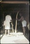 Men mashing food on large wooden bowl