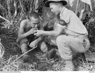 DUMPU, NEW GUINEA, 1943-10-10. NX74107 CORPORAL H.J. MURRAY OF THE 7TH AUSTRALIAN DIVISION PROVOST COMPANY LIGHTING A CIGARETTE FOR A JAPANESE PRISONER, AT HEADQUARTERS, 21ST AUSTRALIAN INFANTRY ..