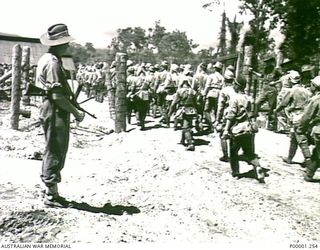 THE SOLOMON ISLANDS, 1949-09-19. AUSTRALIAN GUARDS WATCH AS JAPANESE TROOPS FROM NAURU ISLAND MOVE THROUGH THE GATES OF AN INTERNMENT CAMP ON BOUGAINVILLE ISLAND. (RNZAF OFFICIAL PHOTOGRAPH.)