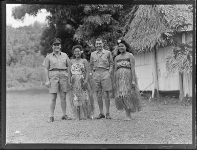 Ron and Stan from RNZAF, with two unidentified local girls in island costume outside a hut, Rarotonga, Cook Islands