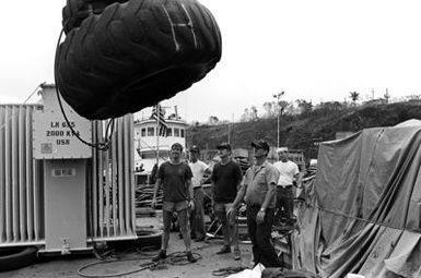 Crewmen aboard the salvage ship USS CONSERVER (ARS-39) prepare to lower tires over the side. The CONSERVER is in port to salvage a Coast Guard boat that sank when hurricane Iwa passed through the area