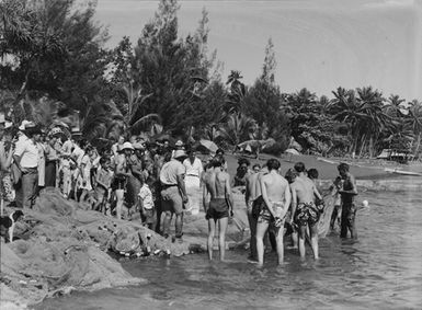 [A large group of onshore tourists watch as local fishers check their nets for catch]