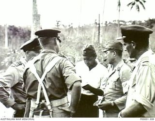 NEW BRITAIN, 1945-09. AN ARMY OFFICER, NEW ZEALAND AIR FORCE OFFICERS AND JAPANESE LIAISON PERSONNEL IN DISCUSSION IN THE RABAUL AREA. (RNZAF OFFICIAL PHOTOGRAPH.)