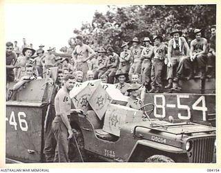 JACQUINOT BAY, NEW BRITAIN. 1944-12-07. GUNNER HARDY, (20), ABOUT TO TRANSPORT AUSTRALIAN COMFORTS FUND CHRISTMAS HAMPERS FROM A BARGE. THE PARCELS WILL BE DISTRIBUTED TO UNITS IN THE AREA DURING ..