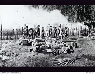 WABAG, NEW GUINEA. 1943-01. CORPORAL TOPMAN (LEFT) AND LIEUTENANT HARRY AIKEN, M SPECIAL UNIT, SERVICES RECONNAISSANCE DEPARTMENT, ALLIED INTELLIGENCE BUREAU, WATCH THE HAUS KUK (COOKHOUSE) GOING ..