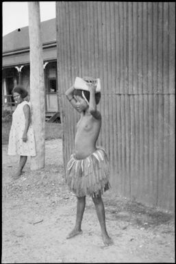 Young girl with a package on her head and a woman watching in background, Awar, Sepik River, New Guinea, 1935 / Sarah Chinnery