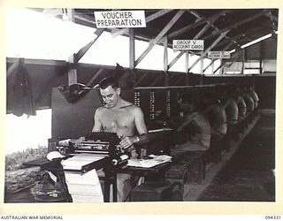 TOROKINA, BOUGAINVILLE. 1945-07-25. PRIVATE L. MUGRIDGE, A TYPIST AT CENTRAL OFFICE, 16 ADVANCED ORDNANCE DEPOT WORKING ON VOUCHER PREPARATION. THE MEN IN THE BACKGROUND ARE AT THE ACCOUNT CARD ..