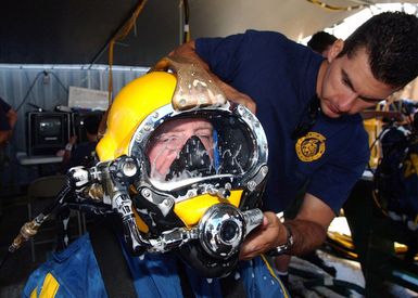 A US Navy diver assigned to Mobile Diving and Salvage Unit One (MDSU-1) uses a soap and water solution, to check for air leaks on the diving helmet of a fellow diver, aboard the Crowley 450-10 barge during recovery operations for the Japanese fishing vessel Ehime Maru off the coast of Hawaii