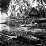 Canoes beached at lagoon shore in slip between reclamations topped by houses