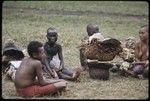 Mortuary ceremony: mourning women with blackened faces and bodies and shaved heads, baskets of banana leaf bundles