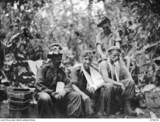 Orderly VX108799 Private Maurice Augustus "Plonk" Hollingsworth, standing, dressing wounded men at the Advanced Dressing Station of the 6th Field Ambulance, Army Medical Corps. The soldier in the ..