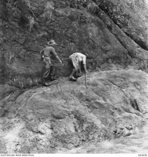 FARIA RIVER, RAMU VALLEY, NEW GUINEA. 1944-01-18. MEMBERS OF THE 2/10TH INFANTRY BATTALION CLAMBERING ALONG THE ROCK-FACED BANK OF THE FARIA RIVER ON THEIR WAY TO GUY'S POST. THEY ARE: SX1461 MAJOR ..