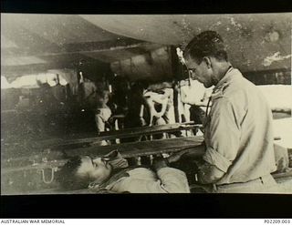 Torokina, Bougainville, New Guinea. 1945-09. A Royal Australian Army Medical Corps (RAAMC) doctor examining a sick Japanese prisoner of war. This soldier and other stretcher cases had recently ..