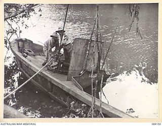 JACQUINOT BAY, NEW BRITAIN. 1944-12-06. CRAFTSMAN W.P. SENIOR, (1), AND SERGEANT A.F.H. CHALKER, (2), 1 INFANTRY TROOP WORKSHOP MEMBERS, RAISE A JAPANESE BARGE FROM THE KULMALALGI RIVER. THE BARGE ..