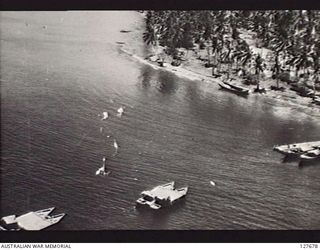 HANSA BAY, NEW GUINEA. 1944-07-31. JAPANESE BARGES AT TEMPORARY WHARF. INVASION BARGE BEACHED IN FOREGROUND. A BOMB CAN BE SEEN BURSTING IN WATER