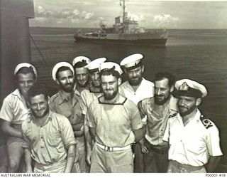 NEW BRITAIN, 1945-09. A GROUP OF AUSTRALIAN SAILORS IN THE RABAUL AREA. BATHURST CLASS MINESWEEPER/CORVETTE HMAS DUBBO IS IN THE BACKGROUND. (RNZAF OFFICIAL PHOTOGRAPH.)