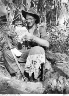 WONGINARA MISSION, NEW GUINEA. 1945-04-04. PRIVATE K.B. WARMINGTON, 2/3 INFANTRY BATTALION, BALANCES A JAPANESE SWORD AND FLAG ON HIS LEGS AS HE READS WELCOME MAIL FROM HOME FOLLOWING HIS RETURN ..