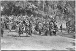 Bride price ritual: decorated men from groom's group dance and sing in bride's village, men in center carry spears in mock aggression