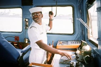 Quartermaster First Class (QM1) Herbert Kelton mans the helm of torpedo retriever boat 10 (TRB-10) as the craft gets underway from the Naval sub base for the day's work