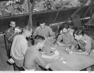JACQUINOT BAY, NEW BRITAIN, 1945-08-31. BATTERY OFFICERS RELAXING IN THE MESS, 141 HEAVY ANTI-AIRCRAFT BATTERY ROYAL AUSTRALIAN ARTILLERY AT A GAME OF CARDS. IDENTIFIED PERSONNEL ARE:- LIEUTENANT ..