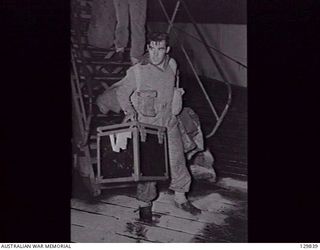 DARLING HARBOUR, NSW. 1946-06-21. VX125715 PRIVATE G. HORSEY CARRIES HIS GEAR IN A BORROWED BOX WHILE DISEMBARKING FROM HMAS MANUNDA AFTER ITS ARRIVAL FROM RABAUL