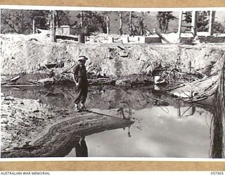 SALAMUA, NEW GUINEA. 1943-09-20. MEMBER OF 162ND AUSTRALIAN LIGHT ANTI AIRCRAFT BATTERY, AIF, STANDING IN THE BOMB CRATER MADE BY AN ALLIED 1000LB BOMB DROPPED BY OUR AIR FORCE ON THE JAPANESE. THE ..