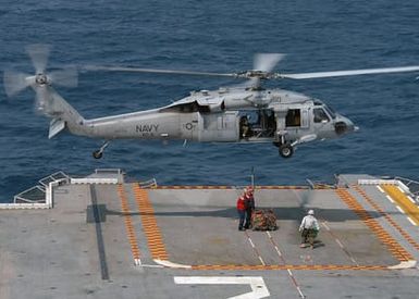 A US Navy (USN) MH-60S Knighthawk, Helicopter Combat Support Squadron 6 (HC-6), Chargers, Naval Air Station (NAS) Norfolk, Virginia (VA), gets hooked up with a bundle of ammunition, bound for a nearby Navy vessel, from the flight deck onboard the Tarawa Class Amphibious Assault Ship USS SAIPAN (LHA 2) during a vertical replenishment (VERTREP) at sea. The SAIPAN is at sea conducting training exercises for a scheduled deployment