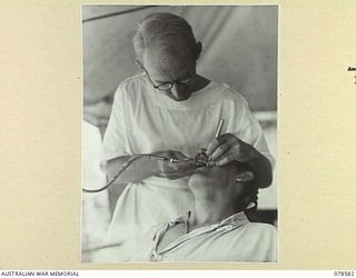 BOUGAINVILLE ISLAND. 1945-01-23. VX133154 CAPTAIN D.F. SPRING, DENTAL OFFICER, FILLING A TOOTH FOR Q105945 PRIVATE MILLER IN THE DENTAL SURGERY OF THE 109TH CASUALTY CLEARING STATION