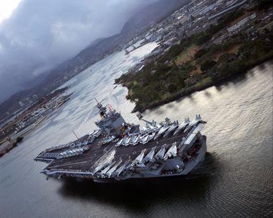 An aerial port quarter view of the nuclear-powered aircraft carrier USS ENTERPRISE (CVN 65) as it enters Pearl Harbor. Members of the crew man the rail