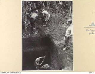 TUNNEL HILL ROAD, RABAUL, NEW BRITAIN. 1945-09-27. TROOPER H.J. WOODGATE, 2/4 ARMOURED REGIMENT STANDS BY WHILE JAPANESE SOLDIERS DIG A DEEP LATRINE PIT AT THE UNIT CAMP