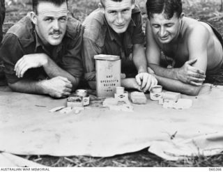 GUY'S POST, FARIA RIVER AREA, NEW GUINEA. 1943-11-08. TROOPS OF THE 2/33RD AUSTRALIAN INFANTRY BATTALION EXAMINING THE NEW FIELD OPERATIONAL RATION. THIS RATION CONTAINS THREE MEALS, EACH WRAPPED ..