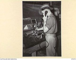 LAE, NEW GUINEA. 1945-03-11. A SIGNALLER OF NO.1 COMPANY, 19TH LINES OF COMMUNICATION SIGNALS TESTING TELEPHONES AND BATTERIES IN THE UNIT STATION