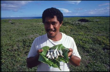 Man holding large leaf covered in small fish