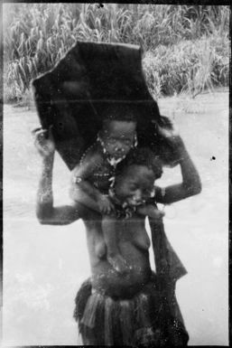 Woman holding a bark rain hood and a child on her shoulders, Ramu River, New Guinea, 1935 / Sarah Chinnery