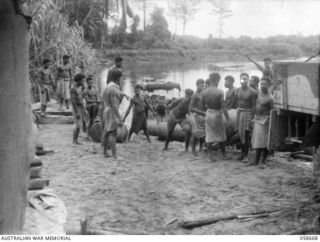 BULLDOG, NEW GUINEA, 1943-09-16. NATIVE LABOURERS TRANSFERRING OIL FROM AN AUSTRALIAN LANDING CRAFT VEHICLE INTO TRUCKS, FOR TRANSPORT TO WAU