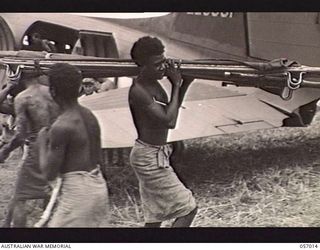 NADZAB AIRSTRIP, NEW GUINEA. 1943-09-18. NATIVES UNLOADING SUPPLIES FROM AIRCRAFT. ON THE RETURN JOURNEY WOUNDED SOLDIERS WILL BE FLOWN BACK TO BASE HOSPITALS