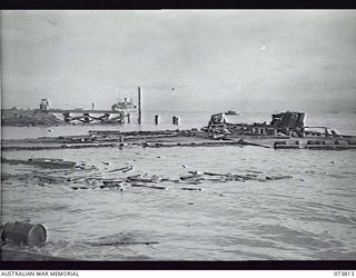 LAE, NEW GUINEA. 1944-06-09. THE REMAINS OF THE WHARF WHICH COLLAPSED AT 0930 ON 1944-06-09. ONE OF THE BARGES SALVAGING DEBRIS IS SEEN WORKING ALONGSIDE THE FLOATING TIMBER