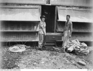 LAE, NEW GUINEA, 1945-05-07. PRIVATE J.H. KILCULLEN (2), HELPING SIGNALWOMAN L.S. BAKER (1), WITH HER TRUNK AT THE AUSTRALIAN WOMEN'S ARMY SERVICE BARRACKS, BUTIBUM ROAD. SHE IS A MEMBER OF A GROUP ..